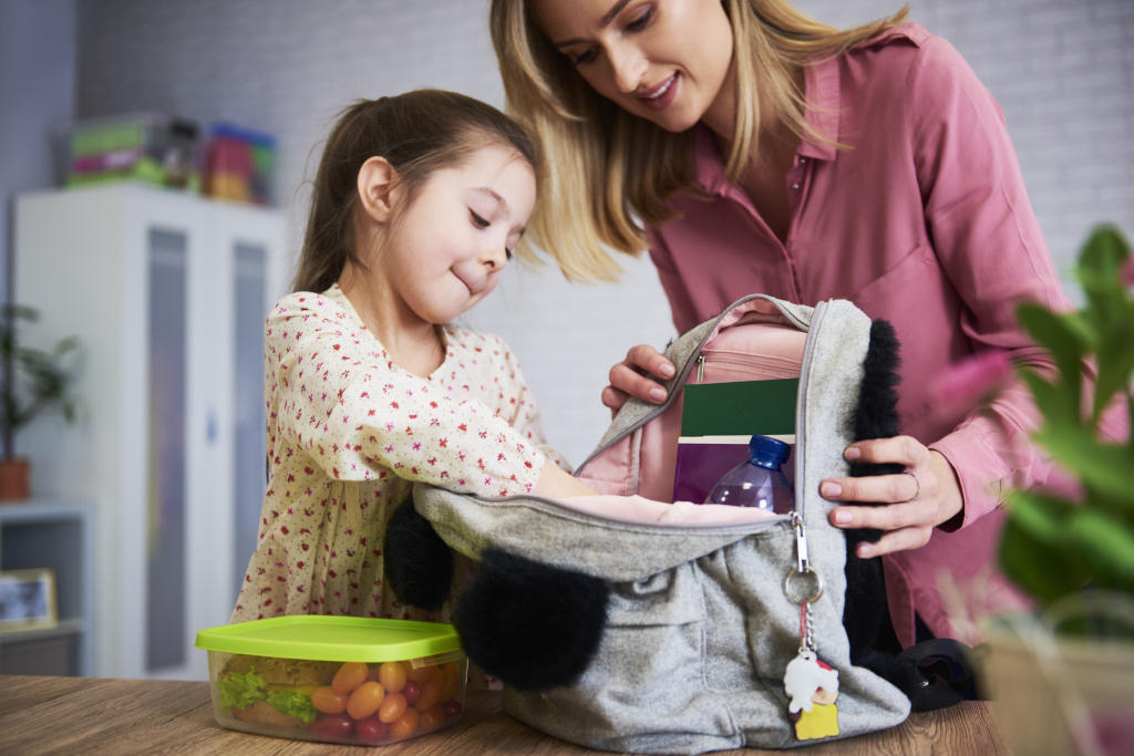 Niña preparando la mochila con su madre, incluyendo el desayuno