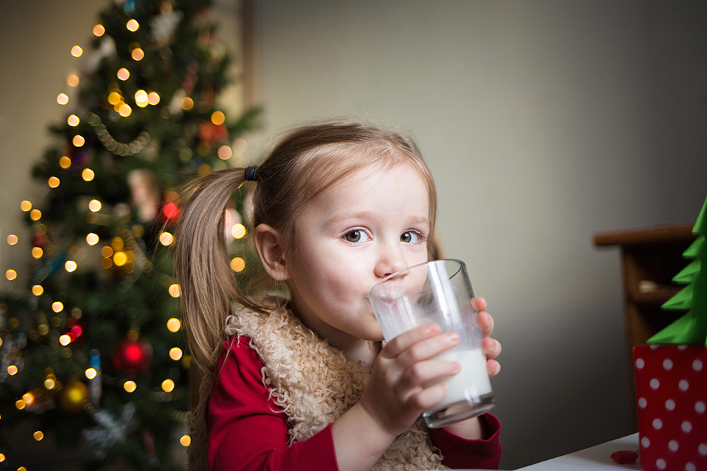 Niña bebiendo leche junto al árbol de Navidad