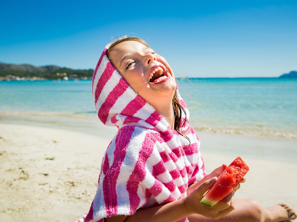 Niña en la playa comiendo sandía